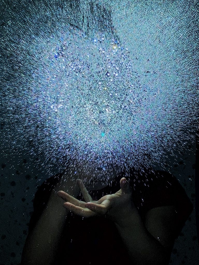 Water droplets on the surface of a mirror glow in the flash of a camera in a mirror. Below, the reflection of a hand appears to hold the drops.