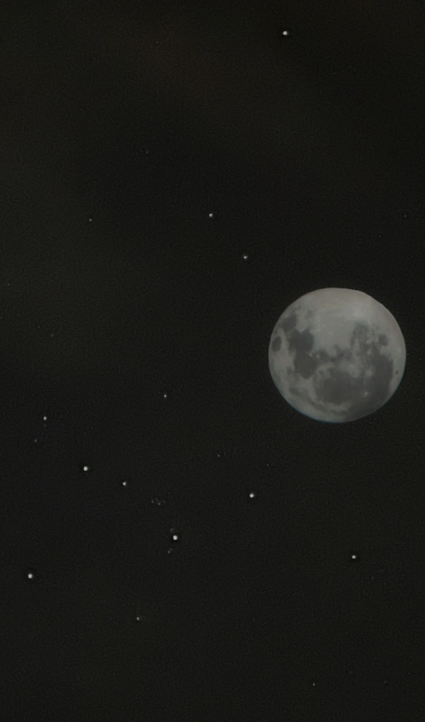 The moon with details of its craters is surrounded by stars shining in the night sky.